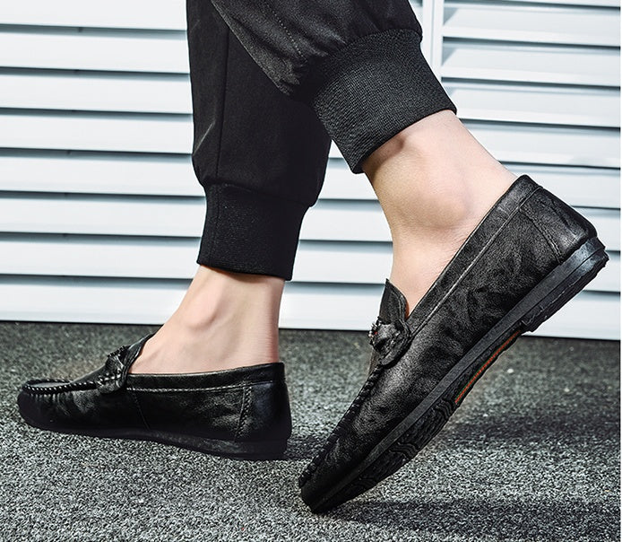 Black moc-toe slip-on loafers on feet, featuring red/gray strap detail