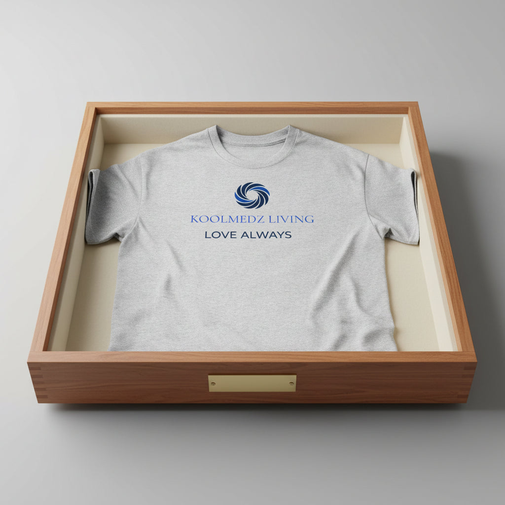A light heather gray short-sleeve t-shirt with a blue and navy graphic on the chest. The graphic features a circular swirl logo above the text 'KOOLMEDZ LIVING' in blue and 'LOVE ALWAYS' in navy, displayed on a clean white background.