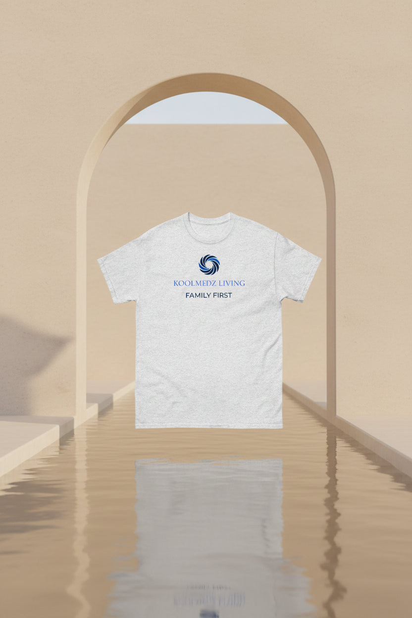 A light heather gray short-sleeve t-shirt with a blue and navy graphic on the chest. The graphic features a circular swirl logo above the text 'KOOLMEDZ LIVING' in blue and 'FAMILY FIRST' in navy, displayed on a clean white background.