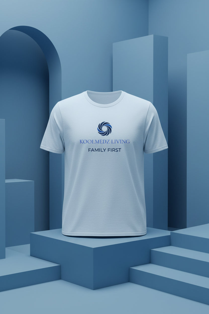 A light blue short-sleeve crewneck t-shirt with a blue and navy graphic on the chest reading 'KOOLMEDZ LIVING FAMILY FIRST' with a swirl logo, displayed on a clean white background.