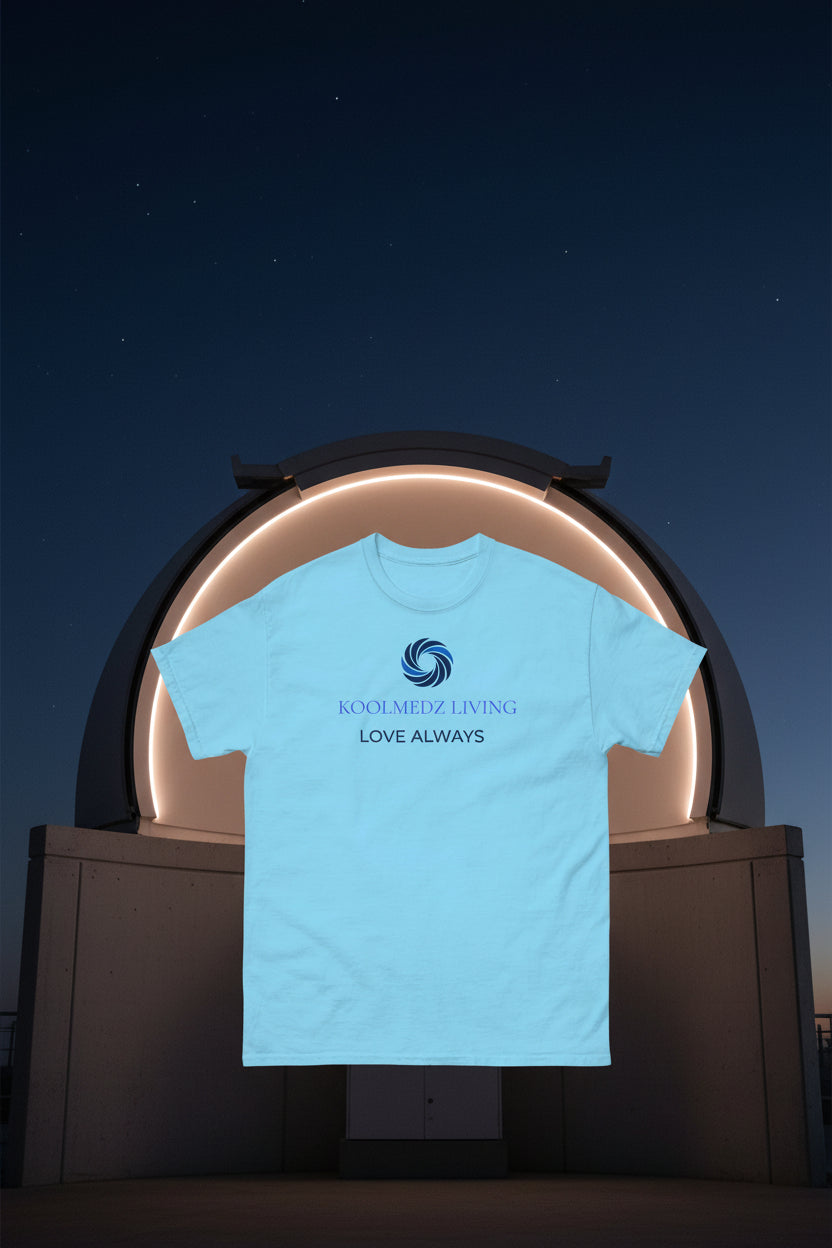 A light blue short-sleeve crewneck t-shirt with a blue and purple graphic on the chest. The graphic features a circular swirl logo above the text 'KOOLMEDZ LIVING' in purple and 'LOVE ALWAYS' in dark blue, displayed on a clean white background.