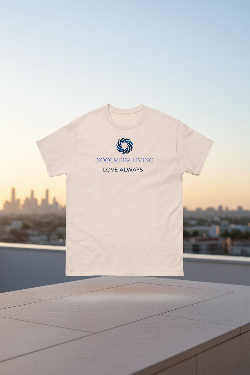 An off-white short-sleeve crewneck t-shirt with a blue and navy graphic on the chest. The graphic features a circular swirl logo above the text 'KOOLMEDZ LIVING' in blue and 'LOVE ALWAYS' in navy.