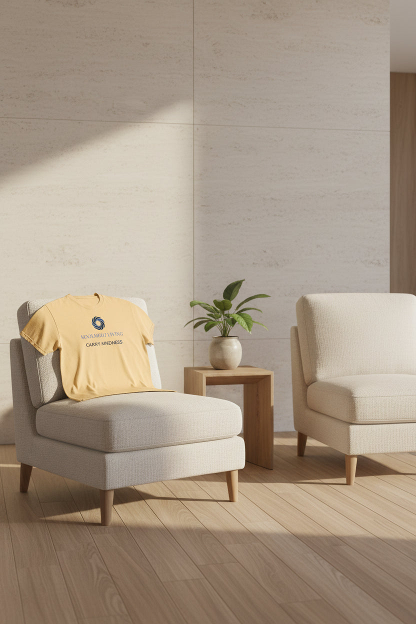 A light peach-beige crewneck t-shirt with a blue and navy graphic on the chest. The graphic features a circular swirl logo above the text 'KOOLMEDZ LIVING' in light blue and 'CARRY KINDNESS' in dark navy.