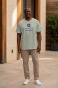 A bay crewneck t-shirt with a blue and navy graphic on the chest reading 'KOOLMEDZ LIVING' and 'ACT KINDLY' with a swirl logo, displayed on a clean white background.