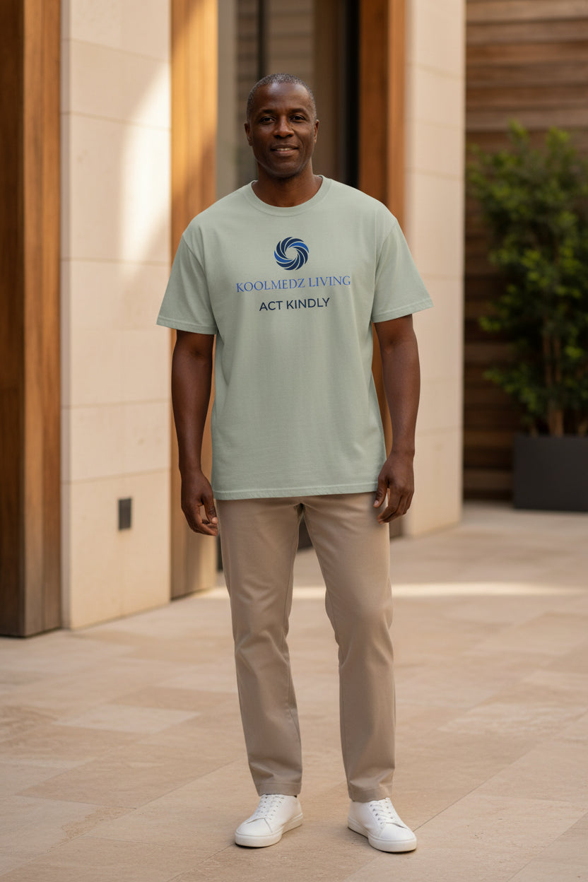 A bay crewneck t-shirt with a blue and navy graphic on the chest reading 'KOOLMEDZ LIVING' and 'ACT KINDLY' with a swirl logo, displayed on a clean white background.